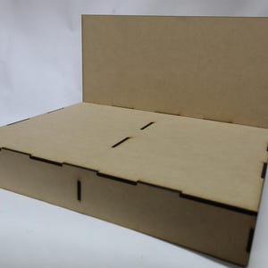 Puede incluir: Un expositor de madera con un panel trasero y una base rectangular. El expositor está hecho de madera marrón claro y tiene un diseño sencillo.