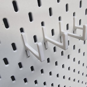 May include: White plastic pegboard hooks, designed to hang items on a pegboard wall. The hooks are in a row, with the ends of the hooks facing the viewer.