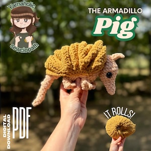 Peut inclure: Un jouet d'armadillo en crochet, surnommé "The Armadillo Pig", est tenu dans une main. Le jouet est brun et beige avec une queue enroulée. Le jouet est étiqueté "IT ROLLS!" et est disponible en téléchargement numérique PDF.