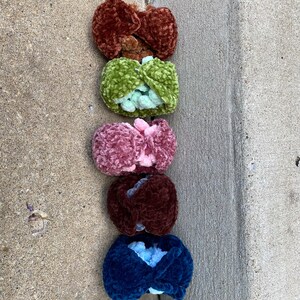 Op de afbeelding: Vijf gebreide haar elastiekjes in verschillende kleuren: bruin, groen, roze, bruin en blauw. De elastiekjes zijn verticaal in een rij gerangschikt.