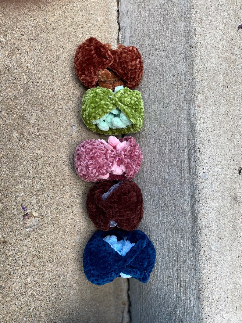 Op de afbeelding: Vijf gebreide haar elastiekjes in verschillende kleuren: bruin, groen, roze, bruin en blauw. De elastiekjes zijn verticaal in een rij gerangschikt.