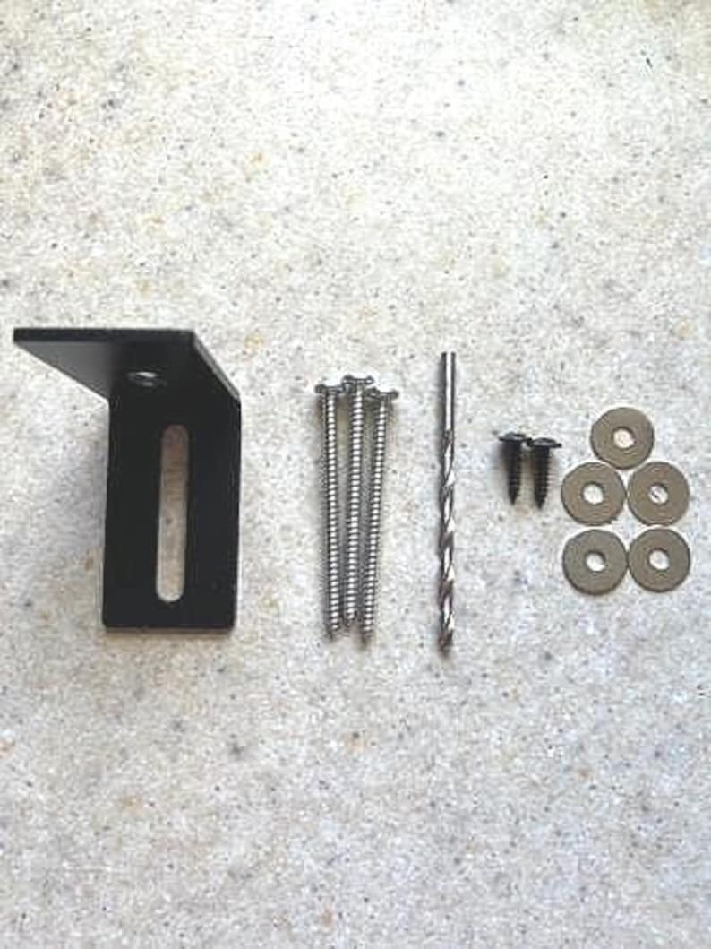 May include: A black metal bracket with a slot for a screw, five silver screws, a silver drill bit, and four silver washers.