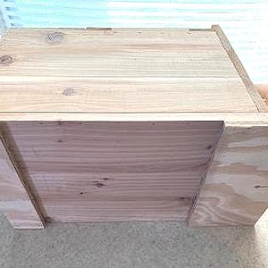 May include: A wooden box with a hinged lid and a plywood back panel. The box is made of unfinished wood and has a natural wood grain.