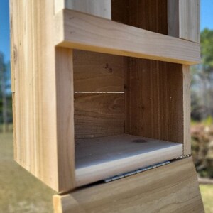 May include: A wooden box with a hinged lid. The box is made of unfinished wood and has a simple design. The box is open and the inside is visible.