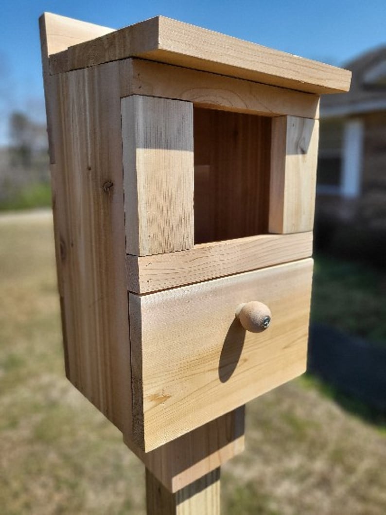 May include: A wooden birdhouse with a small drawer and a knob. The birdhouse is mounted on a wooden post.
