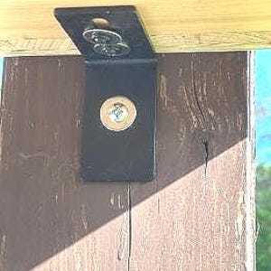 May include: Close-up of a black metal bracket attached to a wooden beam with two screws. The bracket has a rounded edge and a flat surface.