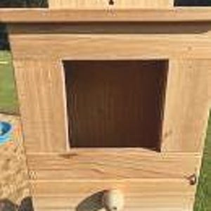May include: A wooden birdhouse with a small opening and a number "1" on the top. The birdhouse is painted a light brown color and has a white knob on the bottom.