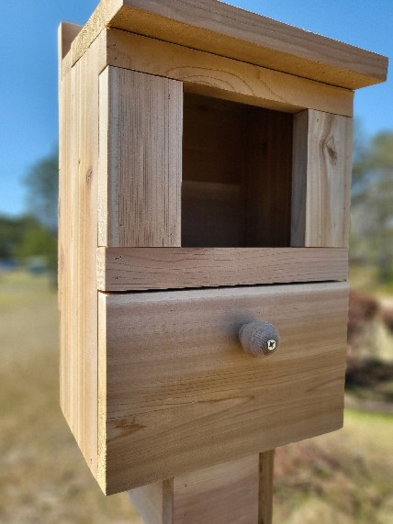 May include: A wooden birdhouse with a small drawer and a knob. The birdhouse is made of natural wood and has a light brown color.