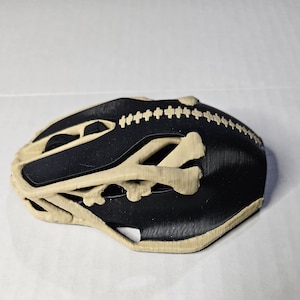 Puede incluir: Casco de bicicleta negro y beige con un diseño esquelético único. El casco presenta un interior negro y detalles exteriores beige, incluyendo estructuras óseas. El diseño es funcional y decorativo, ofreciendo un aspecto distintivo.