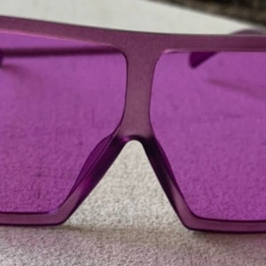 May include: Purple square-shaped sunglasses with a thick frame.