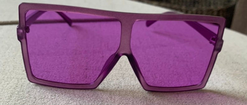 May include: Purple square-shaped sunglasses with a thick frame.