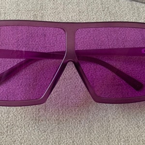 May include: Purple square-shaped sunglasses with a thick frame.