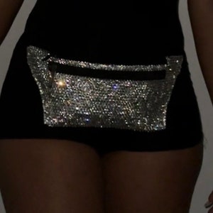 May include: Black shorts with a sparkling, silver rhinestone fanny pack. The fanny pack has a black zipper and is attached to the shorts. The shorts are worn by a person.