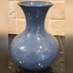 May include: A small, round, blue ceramic vase with a textured glaze. The vase has a narrow neck and a wide base.