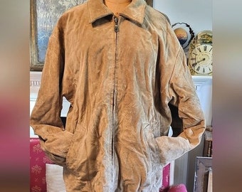 May include: A tan suede jacket with a zip-up front, collared neckline, and two front pockets. The jacket is displayed on a mannequin. The jacket's color is a light brown, and the material appears soft and textured.