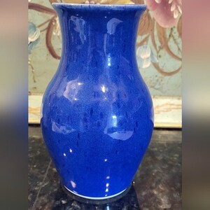May include: A cobalt blue ceramic vase with a rounded body and a narrow neck. The vase has a speckled glaze.