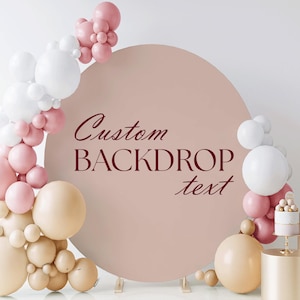 May include: A custom backdrop with the text "Custom BACKDROP text" in burgundy script. The backdrop is surrounded by a balloon arch in white, pink, and beige. A small cake sits on a gold stand.