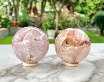 Puede incluir: Dos esferas de ágata rosa y blanca sobre bases de madera. Las esferas tienen un aspecto natural y orgánico con remolinos de color.