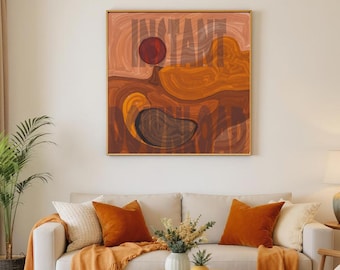 May include: Abstract art print with the word "INSTANT" in a bold font. The artwork features a red circle and swirling shapes in shades of brown, orange, and tan, framed in gold. The print hangs above a cream-colored sofa with orange pillows.