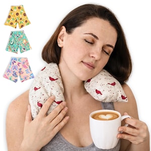 May include: A woman with a neck wrap and a mug of coffee. The neck wrap has a cream background with red bird designs. Three additional neck wraps with different patterns are shown: sunflowers, jungle animals, and butterflies.