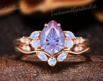May include: A pear-shaped amethyst engagement ring set in rose gold with a halo of smaller diamonds and moonstone accents.