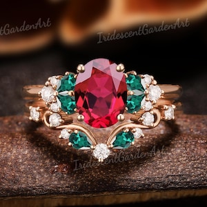 May include: A rose gold engagement ring set with a large oval ruby gemstone surrounded by smaller emerald and diamond stones.