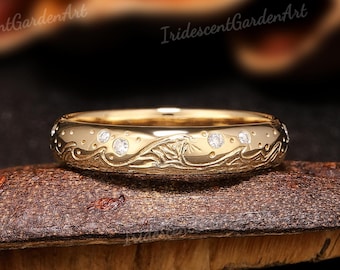 May include: A gold-colored ring with a detailed floral and wave pattern, accented with small, sparkling gemstones. The ring is displayed on a textured, brown surface against a dark background. The text "IridescentGardenArt" is visible.