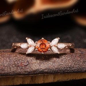May include: A delicate gold ring with a round orange gemstone surrounded by smaller white gemstones in a leaf-like design.