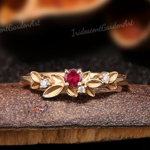 Könnte beinhalten: Ein zarter Goldring mit einem Rubin-Edelstein, umgeben von kleinen Diamanten und blattförmigen Akzenten.