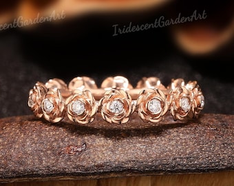 May include: Rose gold ring featuring a floral design. Each flower has a small, sparkling diamond at its center. The ring is set against a dark background, highlighting its intricate details and warm color.