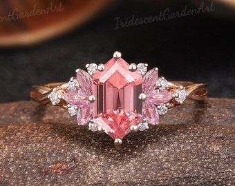 May include: A rose gold engagement ring with a pink octagon-shaped gemstone surrounded by smaller diamonds and pink gemstones. The ring has a twisted band and delicate floral accents.
