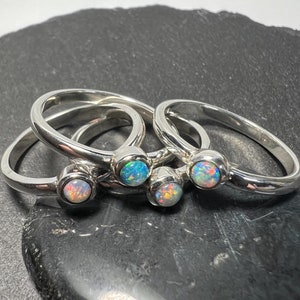 May include: Four silver rings with opal gemstones. The opals are iridescent and have a variety of colours, including blue, green, and pink.