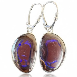 May include: A pair of drop earrings featuring polished, irregular, oval-shaped boulder opals set in silver-toned metal. The stones display a deep brown base color with vibrant, electric blue flashes of color throughout the surface. Each earring is attached to a silver-toned lever-back closure.