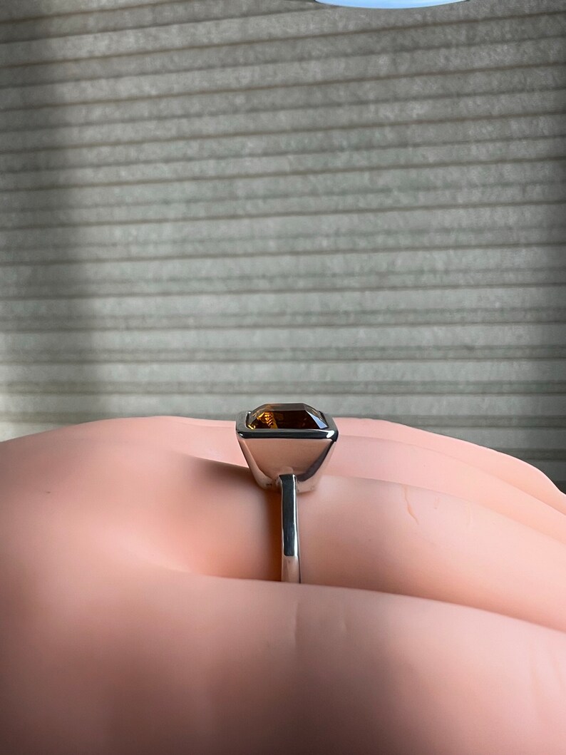 May include: A silver ring with a square-shaped brown gemstone set in a bezel setting.