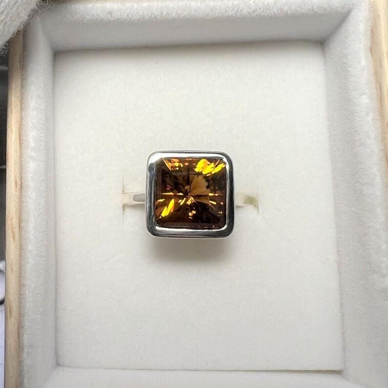May include: A silver ring with a square-shaped, orange gemstone set in a silver bezel.
