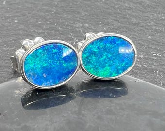 Oval Australian opal stud earrings showing blue and green play of color set in sterling silver.