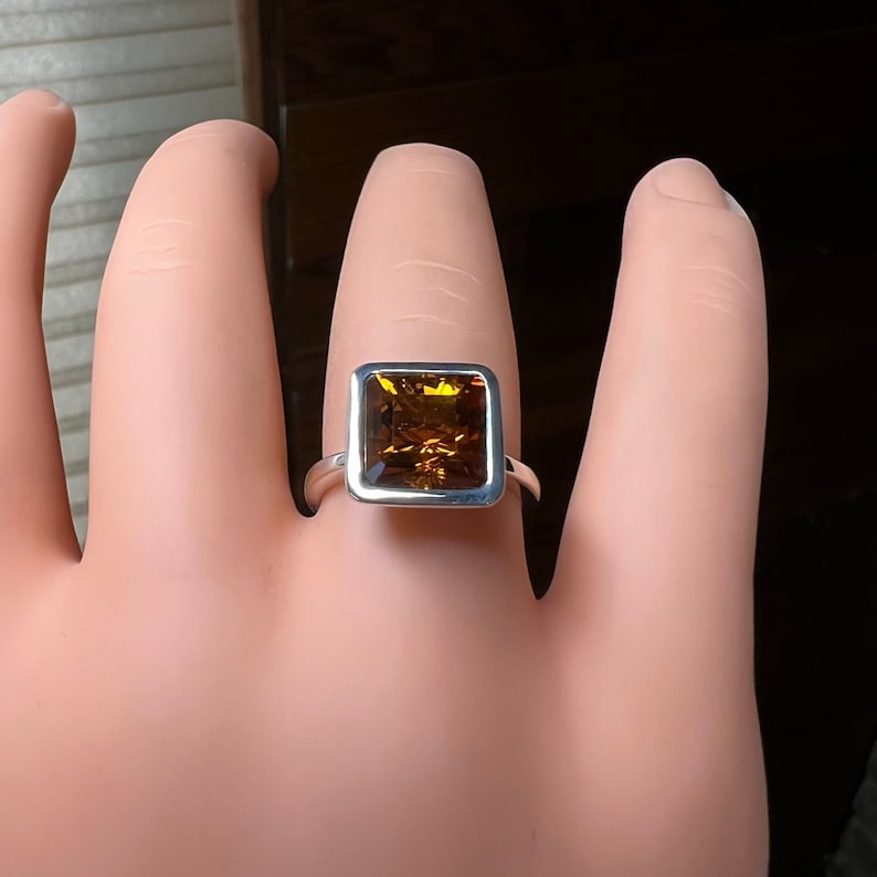 May include: A silver ring with a square-shaped, brown gemstone set in a silver bezel.