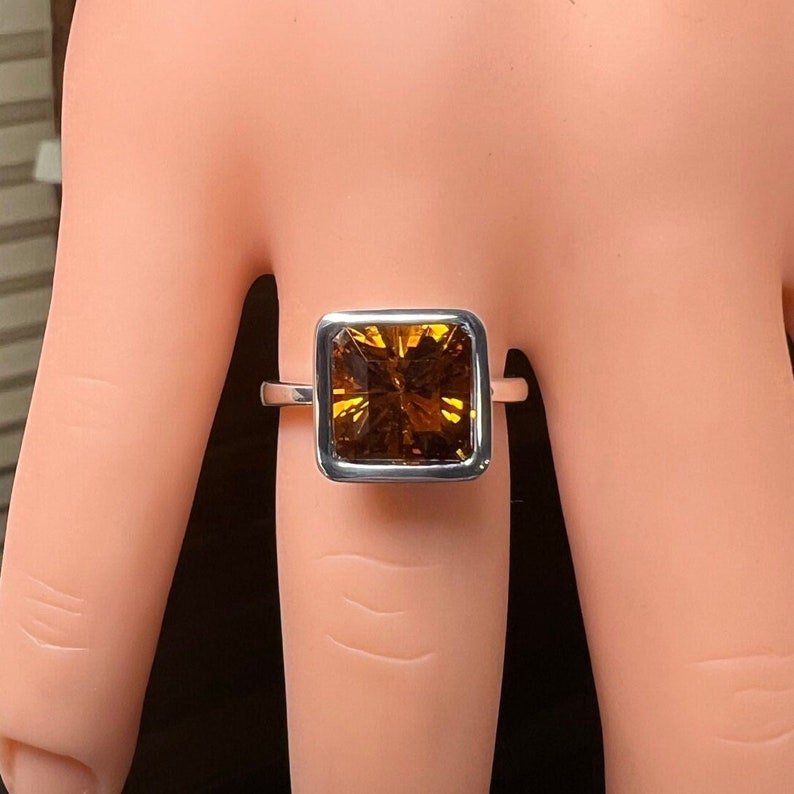 May include: A silver ring with a square-shaped, faceted, amber-colored gemstone.