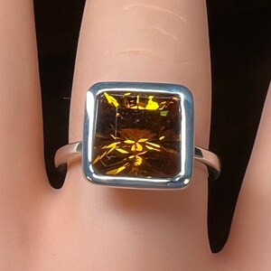 May include: A silver ring with a square-shaped, faceted, amber-colored gemstone.