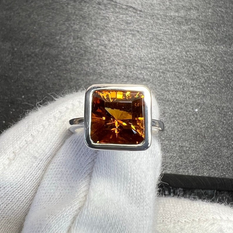 May include: A silver ring with a square-shaped, orange gemstone set in a bezel setting.