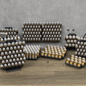 May include: Multiple black metal display stands with rows of small clear glass bottles filled with a light brown liquid. The bottles have white caps. The stands are arranged on a wood floor.