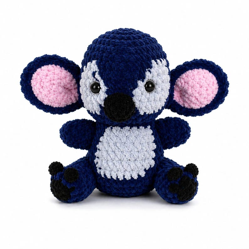 Puede incluir: Un peluche de koala hecho a mano de ganchillo azul y blanco con el interior de las orejas rosa y detalles negros. El koala tiene una barriga blanca y est&aacute; sentado con los brazos y las piernas extendidos. El juguete est&aacute; hecho de hilo suave.