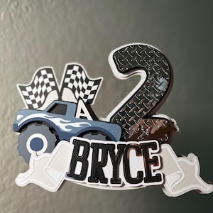 Może przedstawiać: Niebieski topper na tort w kształcie potwora z napisem "Bryce", z flagami w szachownicę i numerem 2.