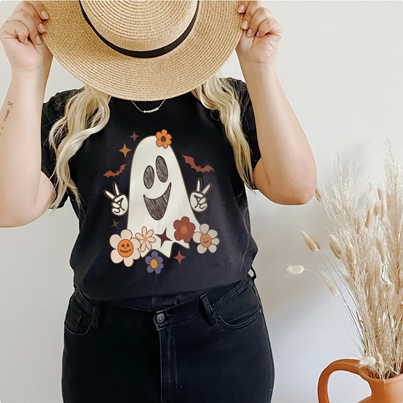May include: Black t-shirt with a white ghost wearing flowers and making a peace sign. The ghost has a happy face and is surrounded by stars.