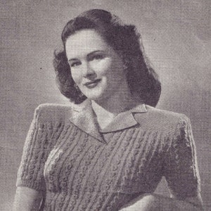 May include: A black and white photo of a woman wearing a cable knit sweater with a collared neckline. The sweater has a textured pattern and short sleeves.