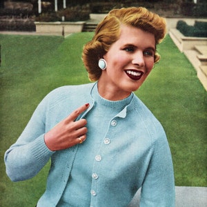 Pode incluir: Um casaco de tricô azul claro com uma blusa combinando. O casaco tem fecho de botões na frente e mangas compridas. A modelo está usando uma saia preta.