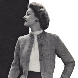 Könnte beinhalten: Graue Strickjacke mit Rundhalsausschnitt und langen Ärmeln. Die Strickjacke hat ein Zopfmuster an den vorderen Kanten und Ärmeln, mit dekorativen Knöpfen. Die Frau trägt eine weiße Bluse darunter.