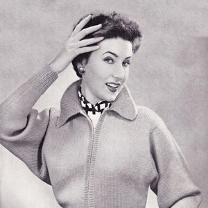 May include: A black and white photo of a woman wearing a light gray knitted cardigan with a zipper closure. The cardigan has a collar and long sleeves. The woman is wearing a black and white checkered scarf and has her hair styled in a short, curly updo.