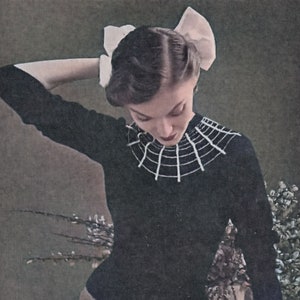 May include: A woman wearing a black sweater with a white crocheted spiderweb collar. She is wearing a white bow in her hair and is looking down at the collar.
