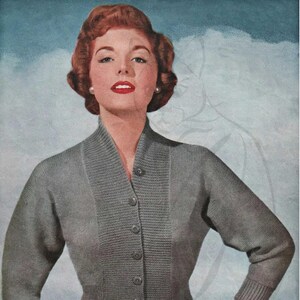 May include: A vintage illustration of a woman wearing a gray cardigan sweater with a button-up front. The sweater has a ribbed texture and a V-neck collar. The woman has red hair and is wearing a dark skirt. The background is a light blue color.